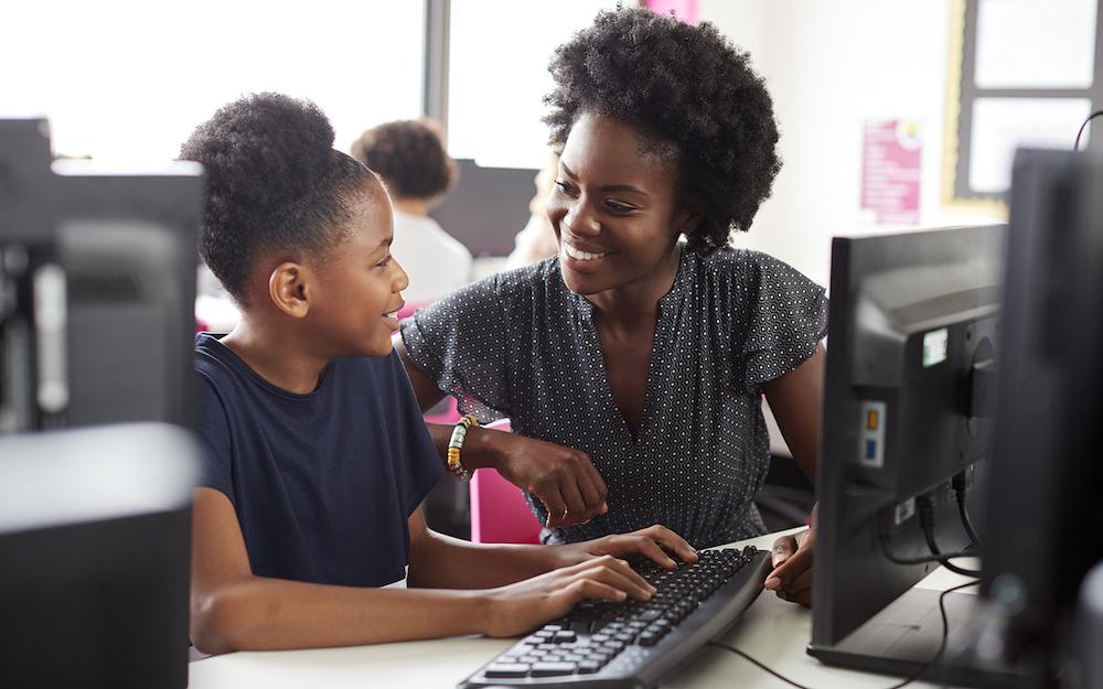 teacher and teen smiling in front of a computer