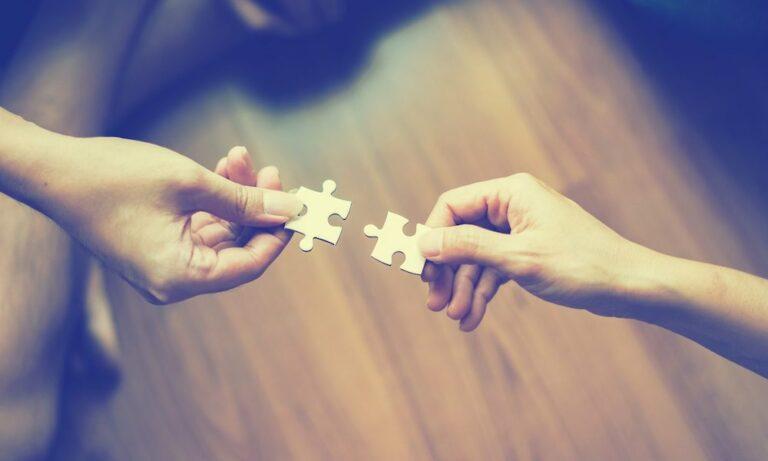 2 hands each with a puzzle piece reaching out to each other