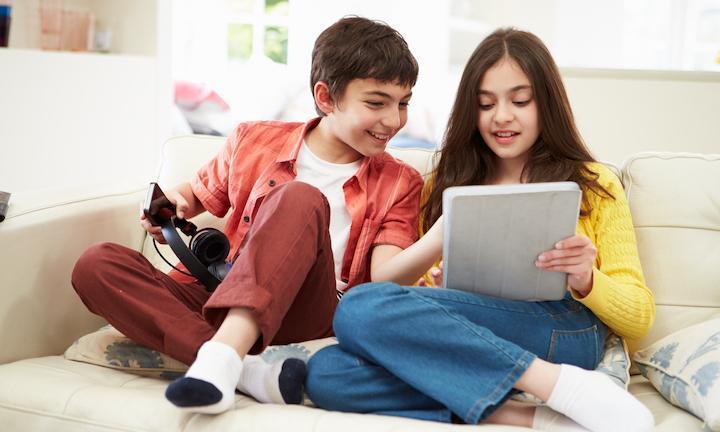 brother and sister on couch looking at tablet computer together