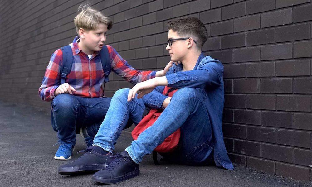 teen kneeling down to talk with another teen outside of school