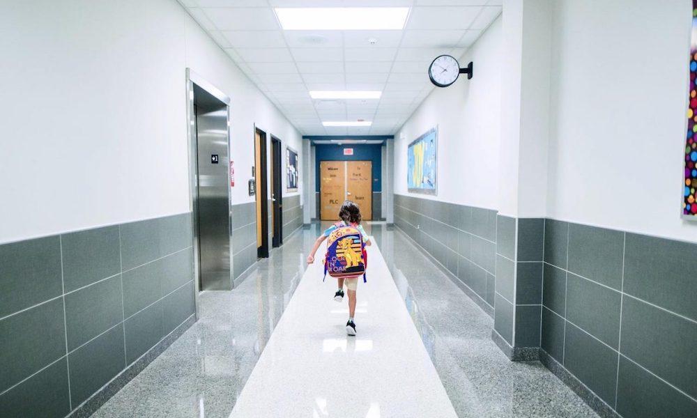 elementary school student wearing a backpack and walking alone down a hallway