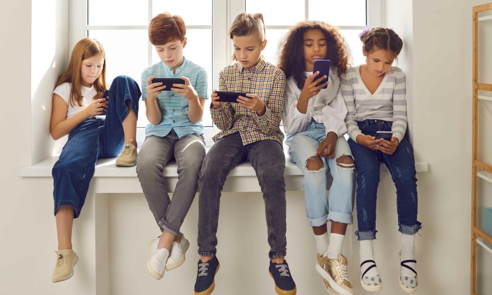 row of young teens sitting in a window sill and looking at their mobile devlces
