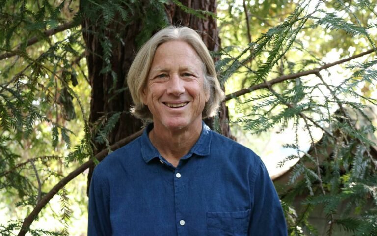 smiling photo of Dacher Keltner standing in front of an evergreen tree