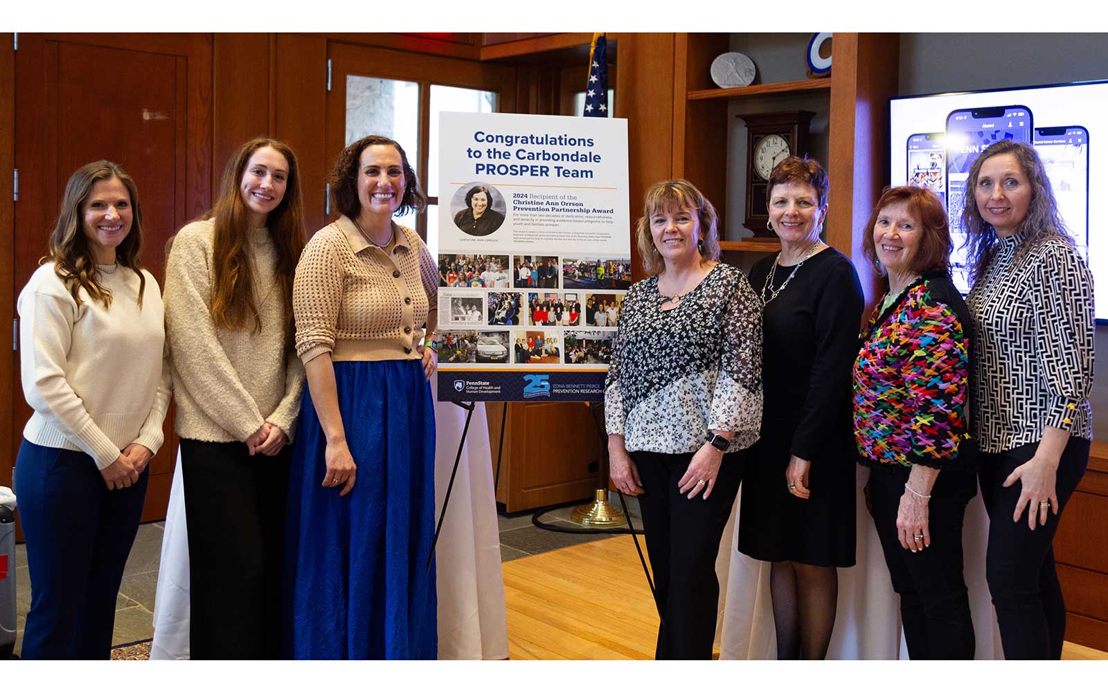 7 smiling woman standing next to a poster announcing the Carbondale PROSPER award